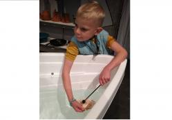 Un enfant tape avec une baguette sur un coquillage posé à la surface de l'eau pour produire un son